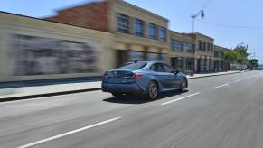 A blue 2025 Toyota Camry hybrid shows off its rear-end styling as it cruises a city street.