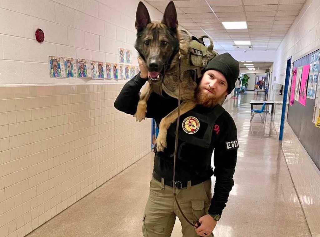 Man wearing a uniform stands in a hallway with a German Shepherd sitting on his shoulder.