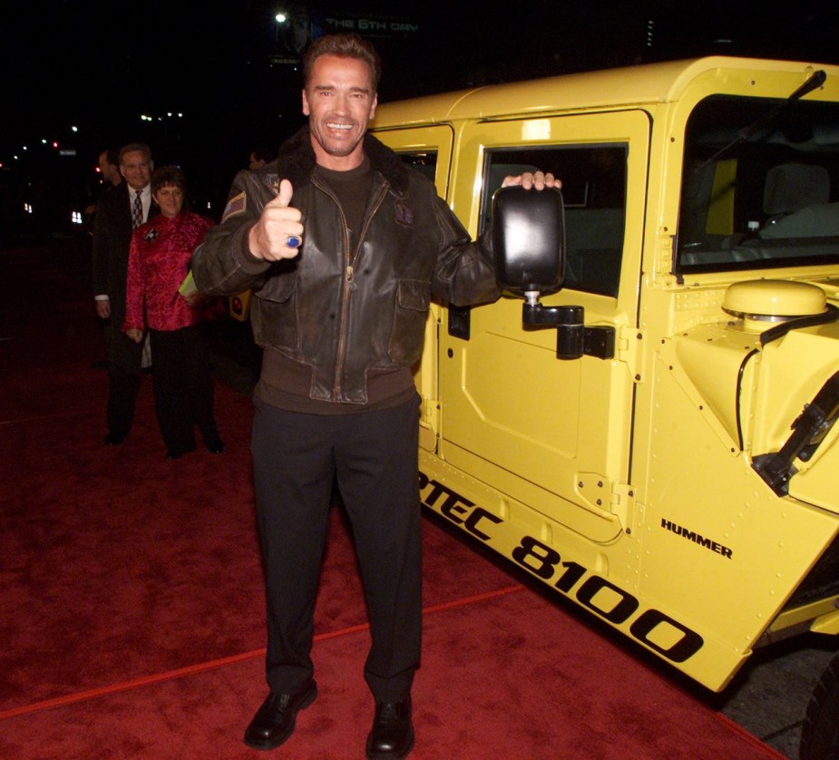 Movie star arnold schwarzenegger gives a thumbs up, standing next to his yellow Hummer H1