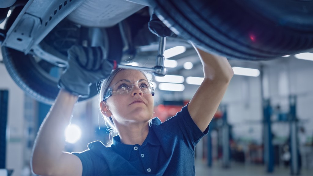 An automotive technician with a ratchet tightens a bolt beneath a car