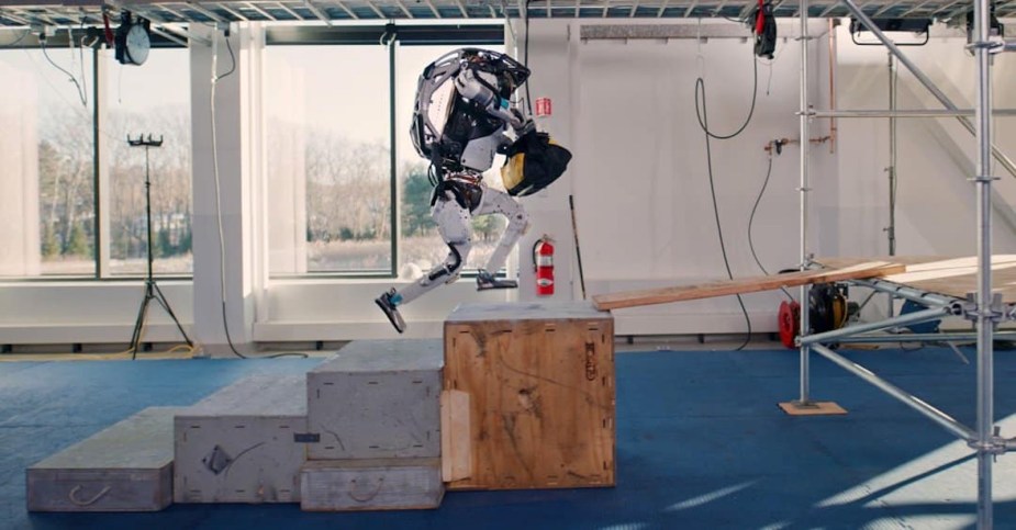 A white humanoid Boston Robotics robot climbing up a set of stairs.