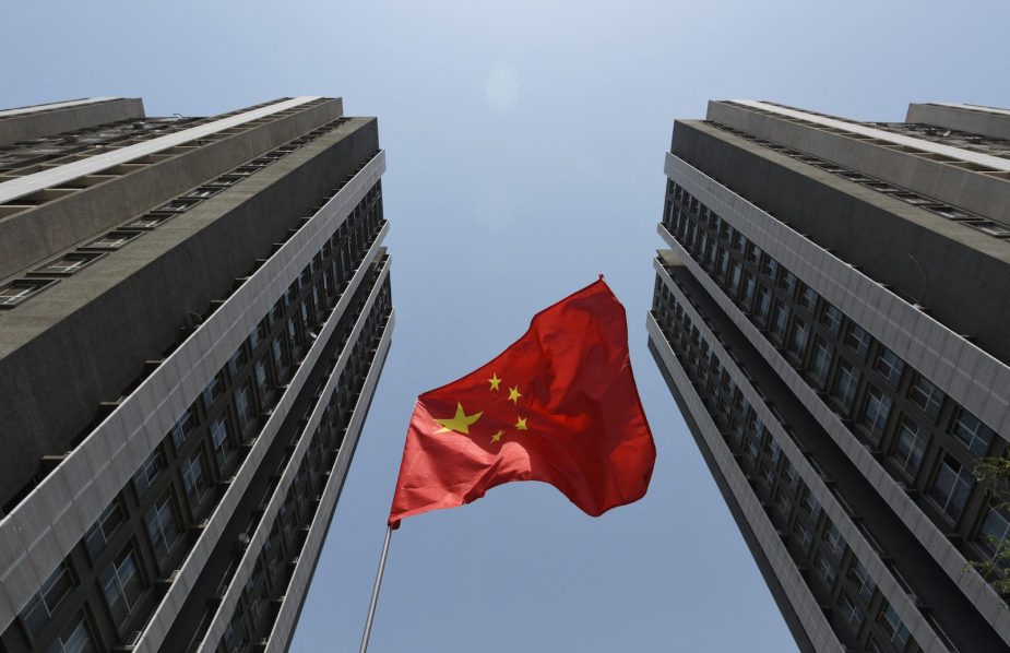 A red Chinese flag between two skyscrapers.