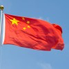 China's red flag with yellow stars flying in front of a blue sky