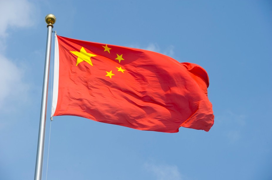 China's red flag with yellow stars flying in front of a blue sky