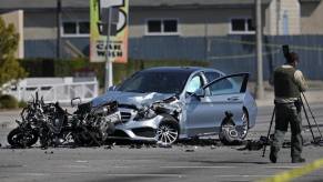 Wreckage of a motorcycle smashed into a silver Mercedes sedan, a police officer in the foreground