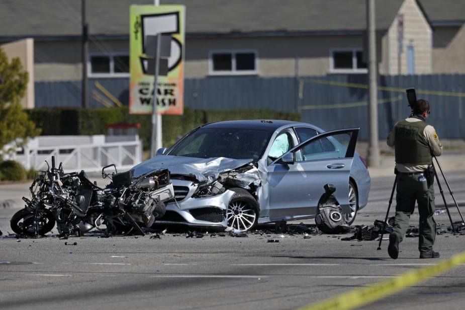 Wreckage of a motorcycle smashed into a silver Mercedes sedan, a police officer in the foreground