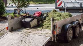 A lawn mower sits on a professional lawn service's trailer with clippings.