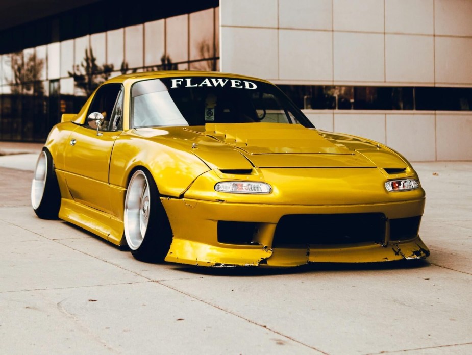 Golden yellow NA Miata on lowered suspension with stanced rims.