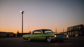 Green classic car on lowered suspension parked in front of the sunset.
