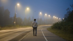 Young man walks under a row of street lights on a road at night.