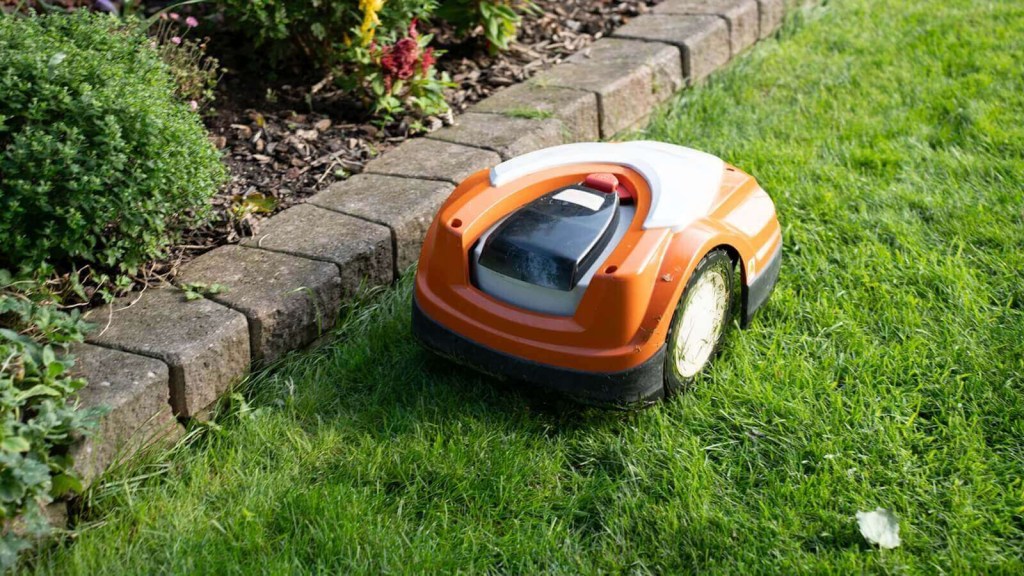 A robot lawn mower mows a lawn next to a little wall.