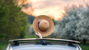 A passenger waves their hat through an open sunroof in a car.