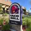 The "Taco Bell Drive Through" sign outside a restaurant, plants visible in the background.
