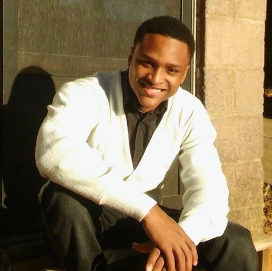 Young man in white jacket sits and smiles for a portrait.