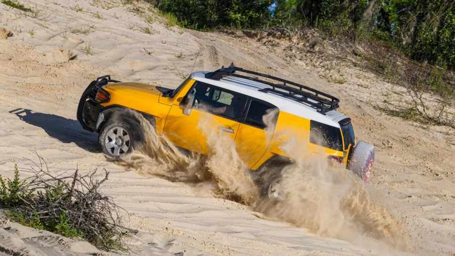 Yellow Toyota FJ Cruiser SUV drives up sand dunes on the beach.