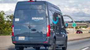 A blue Amazon delivery van facing away from viewer driving on the highway