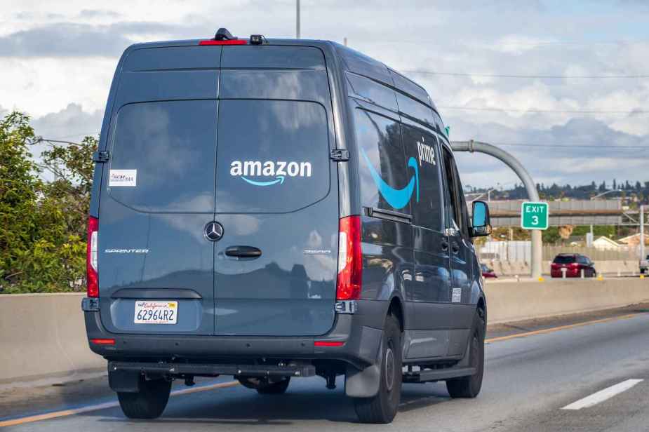 A blue Amazon delivery van facing away from viewer driving on the highway