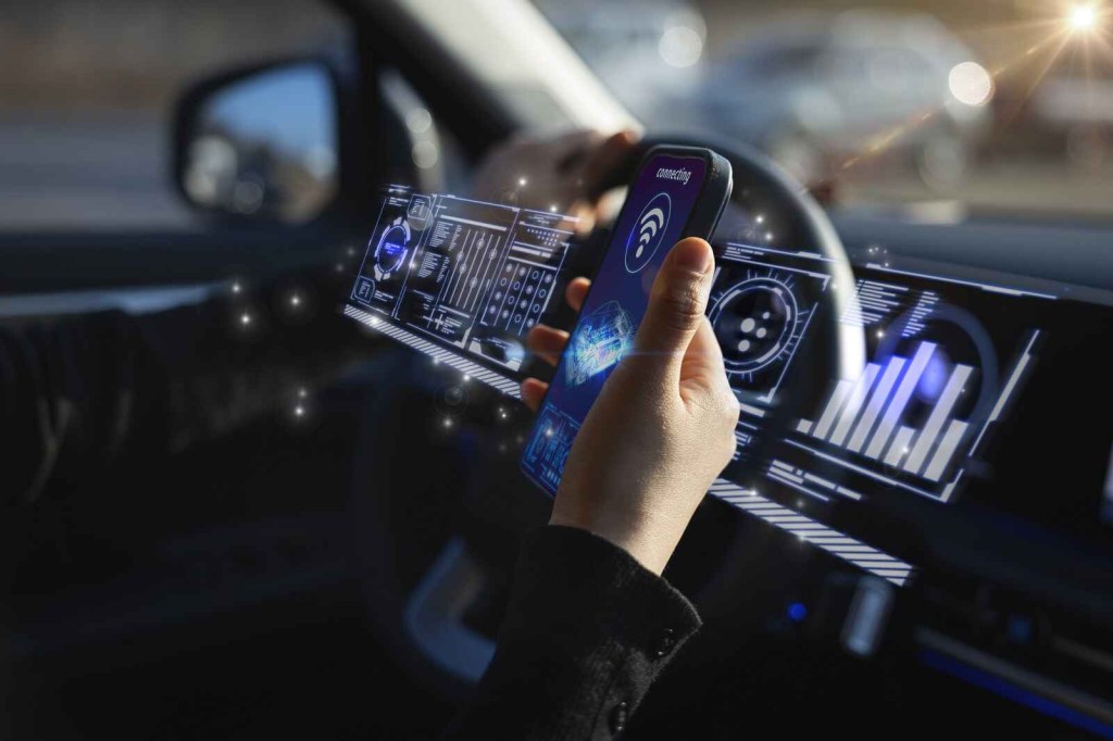 A hand holding a cell phone connecting to car infotainment large full screen across dashboard rendering