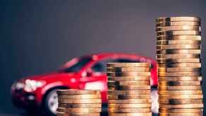 A red toy car shown blurred behind a stacks of gold coins