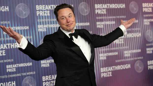 Elon Musk Tesla CEO wearing a black tuxedo at an event with arms open wide smirking closed smile