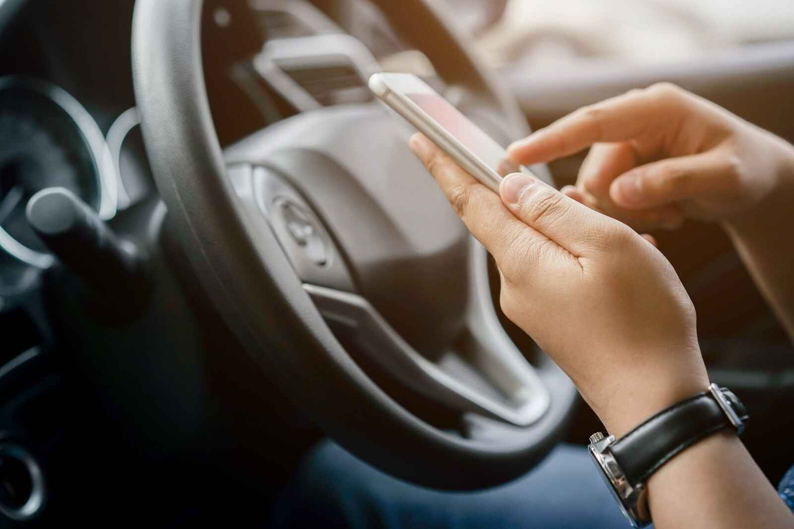 Someone's hands wearing black watch on left wrist texting while in the drivers seat of a car shows how one might break a hands-free state law