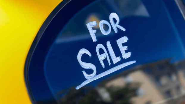 The words "for sale" are written in white paint marker on a yellow car's window in close view