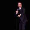 Comedian Jerry Seinfeld on stage performing in black suit