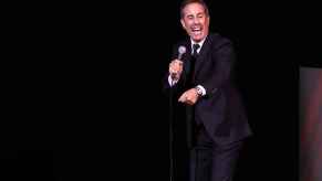 Comedian Jerry Seinfeld on stage performing in black suit