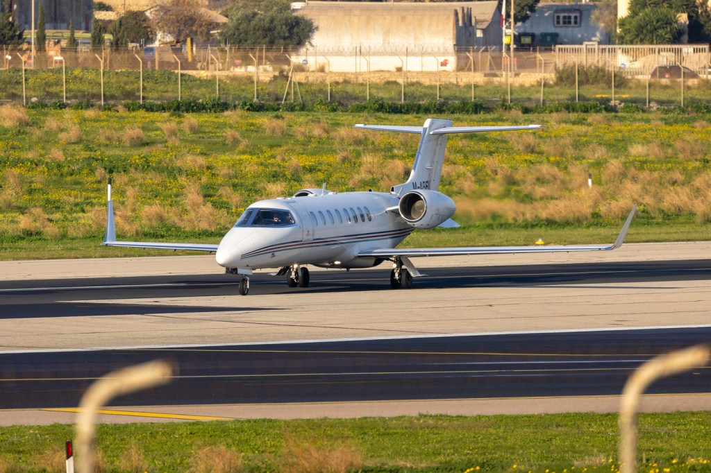 A white Learjet business plane driving down a runway in left front profile view