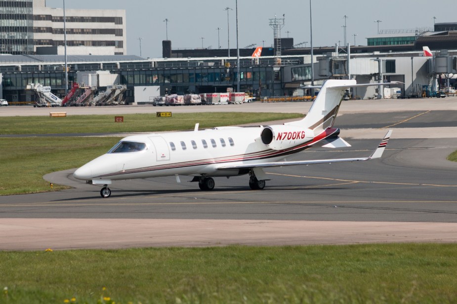 A white Learjet plane shown in left front profile view waiting at an airport tarmac
