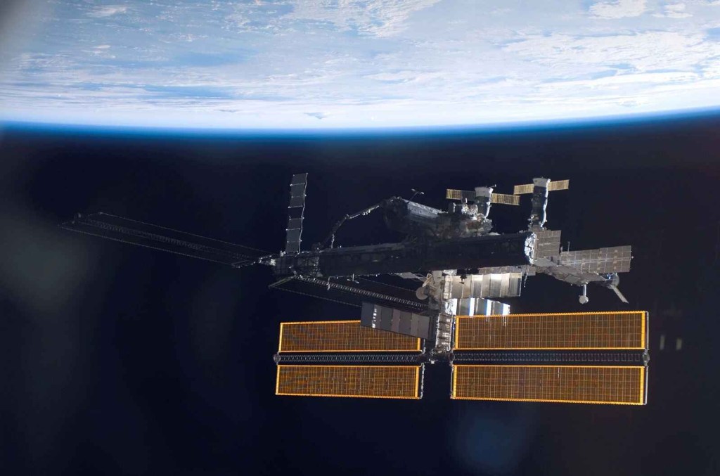 The International Space Station in full view in right lower frame with Earth above