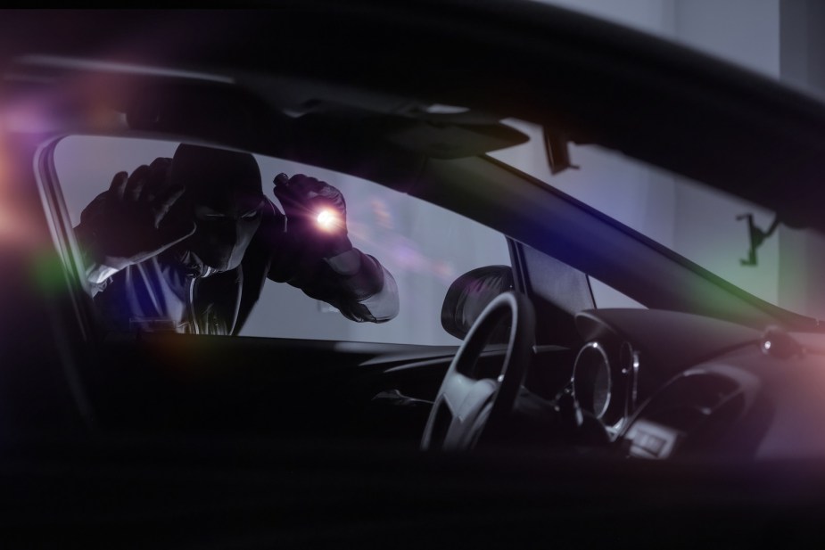 Car thief looking through a window with a flashlight to prepare for a relay attack