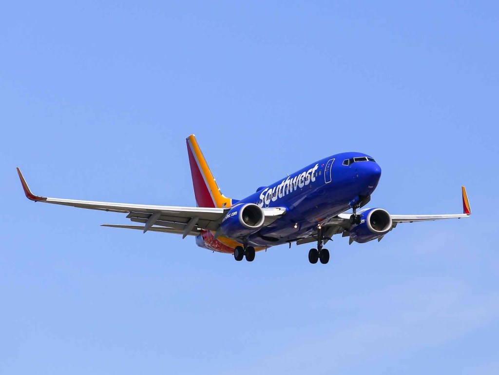 A Southwest Airlines commercial Boeing plane flies in a bright blue cloudless sky