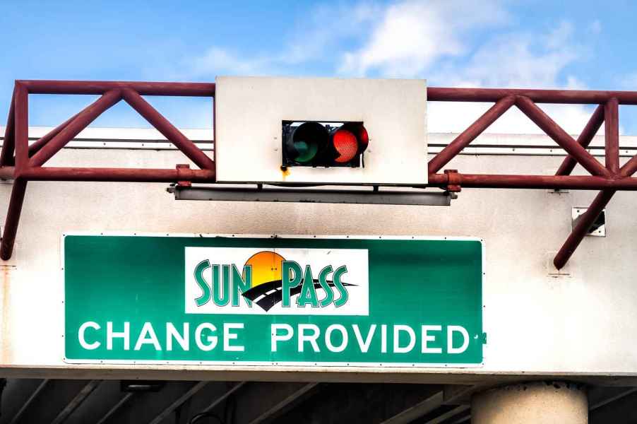 A green sign posted under a stop/go traffic light with the SunPass logo and words "change provided"