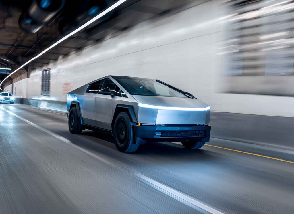 A Tesla Cybertruck EV pickup is shown driving fast at night in an urban setting