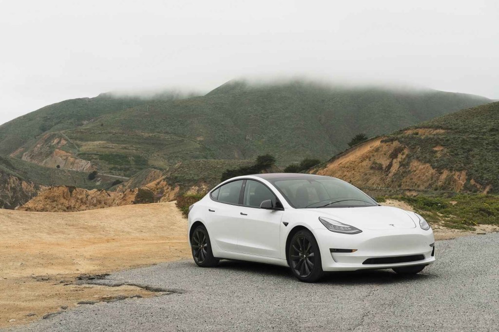 A white Tesla Model 3 parked in a foggy mountain location in right front angle view