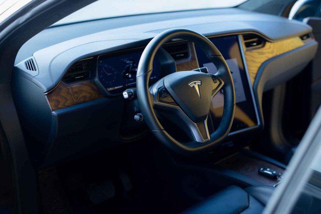 The black front interior of a Tesla EV car shown from open left front door
