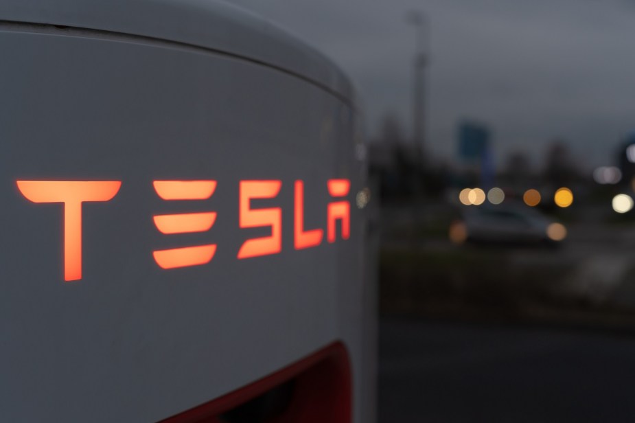 Tesla supercharger in very close top view at night with "Tesla" logo backlit in orange lighting