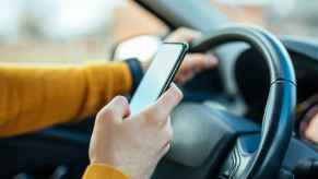A set of arms wearing mustard yellow shirt driving a car while texting on cell phone showing distracted driving and violation of hands-free states laws