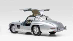A silver 1955 Mercedes-Benz 300SL Gullwing with doors open parked in left ear angle view on white surface white background