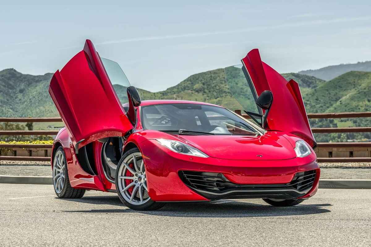 A red 2012 McLaren 12C coupe parked in right front angle view with open gullwing doors