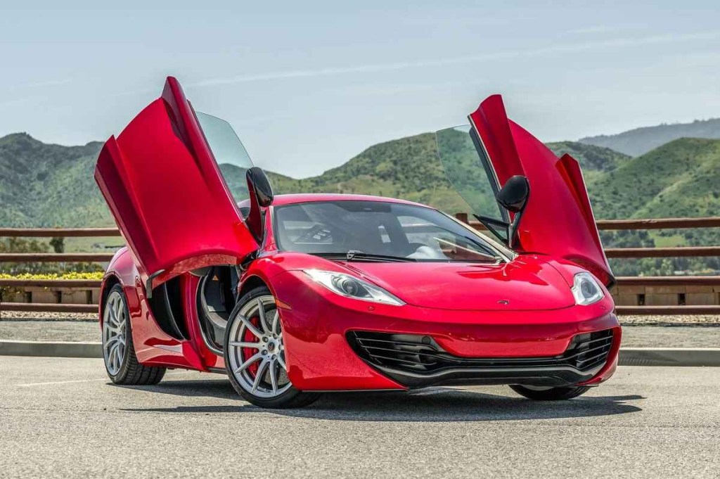 A red 2012 McLaren 12C coupe parked in right front angle view with open gullwing doors