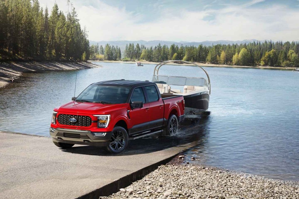 A red and black 2023 Ford F-150 Heritage Edition backing a loaded boat trailer into a lake.