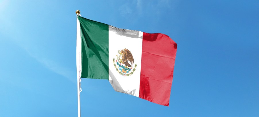 Mexican flag on a pole, a blue sky visible in the background.