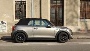 Gray mini cooper convertible with a black top parked on a city street.