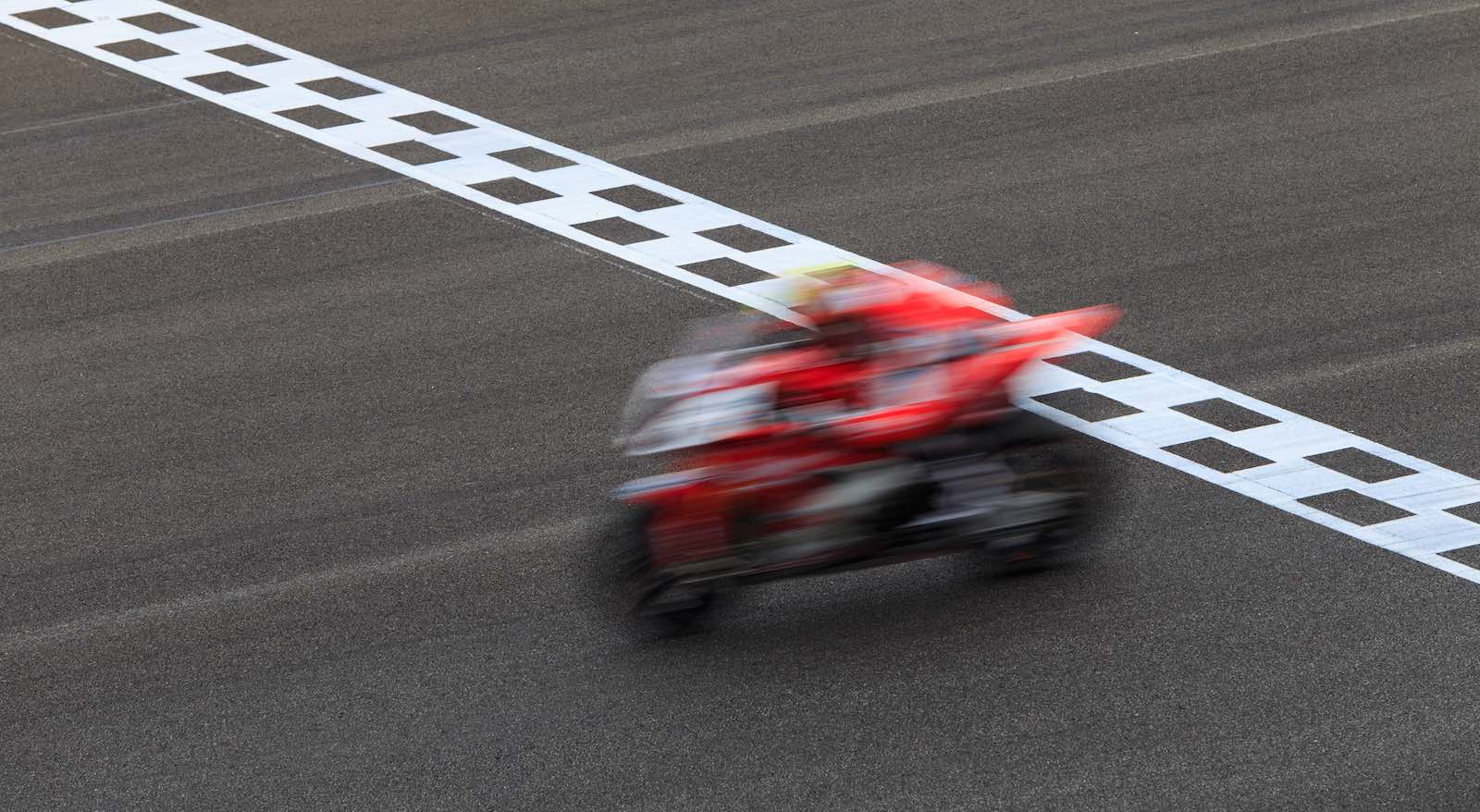 Red motorcycle superbike crossing a finish line during a race.