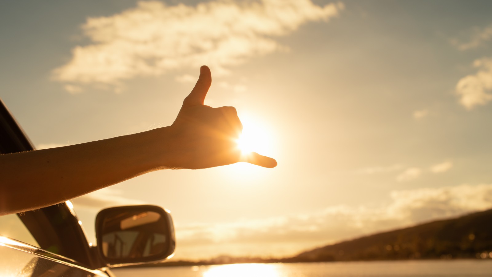 Shaka Hand Sign Out the Window of a Car with the sun setting behind it