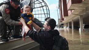 A Texas Game Warden on an airboat bends over to rescue a baby trapped by floodwaters