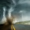 A tornado touches down on a rural road while lightning strikes in the distance