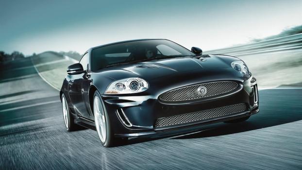 An X150 Jaguar XKR dashes around a corner on an empty road.